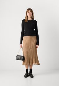 Černý svetr z pleteniny, béžová midi sukně s ribbed vzorem, černá kabelka přes rameno se zlatým řetězem a černé dřeváky. Jednoduchý, texturovaný a vrstvený vzhled.