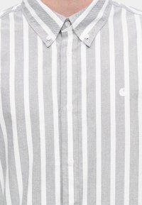 Γκρι και λευκό ριγέ πουκάμισο με κουμπιά και κλασικό γιακά, με μικρό λογότυπο στο στήθος και υφασμα με υφή.