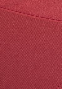 Tecido elástico numa tonalidade de vermelho profundo, apresentando uma superfície texturizada com nervuras diagonais. Detalhe da costura visível ao longo da borda.