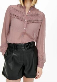 Dusty mauve blouse with textured polka dots, high collar, and button front. Paired with black faux leather high-waisted shorts with belt.