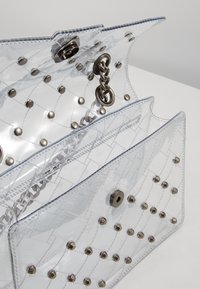 Borsa a mano in plastica trasparente con motivo trapuntato, accessori in metallo argentato e borchie metalliche. Presenta una tracolla a catena e chiusura a scatto.