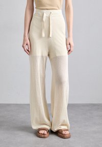 Pantalons larges en tissu en maille beige clair avec une taille haute et un cordon ajustable. Accentués par des sandales plates texturées.