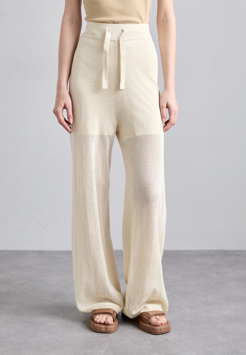 Pantalons larges en tissu en maille beige clair avec une taille haute et un cordon ajustable. Accentués par des sandales plates texturées.