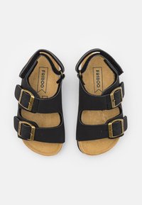 Svarte sandaler med to justerbare spenner, med en korksåle og åpen design for ventilasjon. Glatt materiale og flat såle.