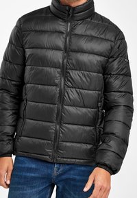 Giubbotto a vento nero con colletto alto, caratterizzato da sezioni scucite orizzontali, due tasche laterali con zip e polsini elasticizzati per una vestibilità aderente.