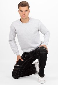 Felpa grigia con maniche lunghe e collo rotondo; abbinata a jeans neri con cerniere e cuciture bianche; modello in ginocchio senza accessori.