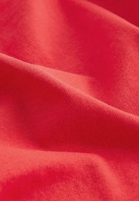 Tissu en coton rouge avec une texture lisse, affichant des plis et des rides prononcés pour une apparence dynamique et une répartition uniforme des couleurs.