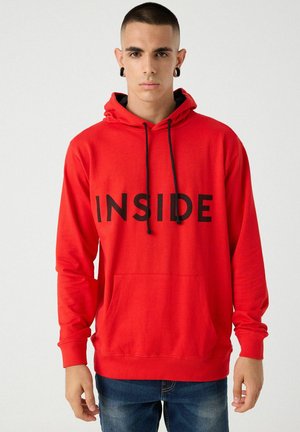 Sudadera roja con cordones negros y gran texto "INSIDE" en la parte frontal. Cuenta con un bolsillo tipo canguro y puños acanalados. Textura de tela suave.