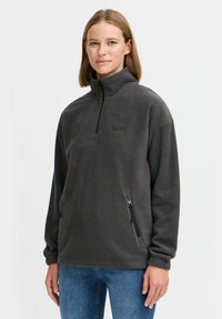 Pullover in pile grigio scuro con colletto alto, chiusura con zip frontale e tasche laterali. Presenta un piccolo logo sul petto e polsini a costine.