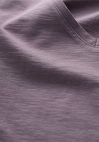 Primo piano di un morbido tessuto di lavanda con texture, cuciture visibili e un sottile dettaglio cucito a forma di V.