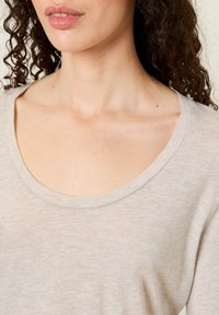 Svetlo béžové tričko s širokým výstrihom, vyrobené z mäkkej látky s hladkou textúrou, s krátkymi rukávmi a voľným strihom.