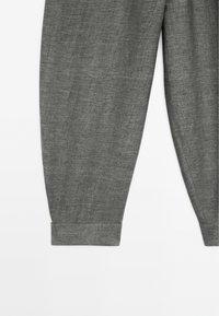 Partie inférieure d’un pantalon gris texturé avec ourlets retroussés sur fond blanc.