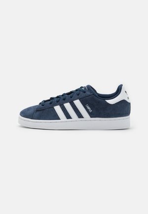 Basket Adidas Campus bleu marine avec des bandes blanches, semelle blanche et languette de talon blanche avec logo, vue de profil sur fond uni.