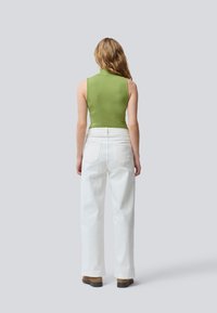 Top sans manches vert à encolure haute associé à un jean large blanc, avec une taille haute et coupe droite. Bottines marron.