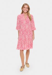 Rosa klänning med vitt blommönster, knäppt placket, 3/4 ärmar och utsvängd nederkant. Matchad med beige platta skor.