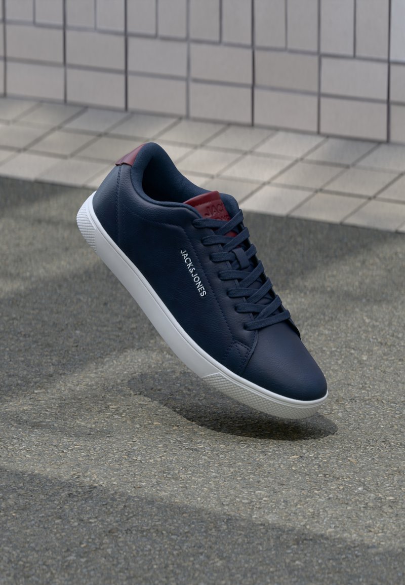 Marineblaue Leder-Sneaker mit einer weißen Gummisohle, runder Zehenform, Schnürdesign und roten Akzenten an der Ferse und der Zunge. Markenlogo sichtbar.
