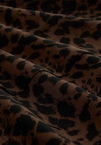 Tissu marron avec un motif léopard noir, présentant une texture douce et des plis délicats, mettant en valeur le contraste entre les couleurs.