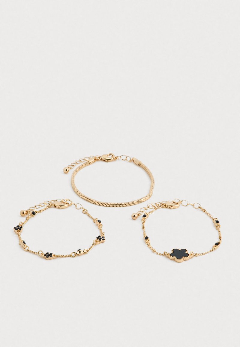 Tričko zlatých náramkov, z ktorých dva obsahujú čierne kvety v tvare kvetov, usporiadané na bielom pozadí.