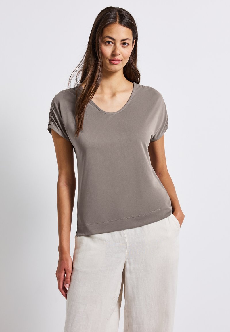 T-shirt gris à encolure dégagée en tissu lisse avec des manches courtes repliées, associé à un pantalon en lin crème clair, doté de poches latérales.