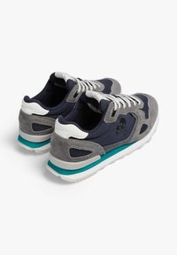 Zapatillas de ante gris y marino con malla, cordones blancos y un acento en teal en la suela. Presentan un gráfico de calavera en el lateral.