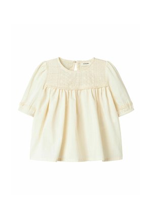 Lichtbeige katoen blouse met een getextureerde schouderpas, gathered lijfje en elastische manchetten. Heeft een keyhole sluiting aan de achterkant voor eenvoudig aantrekken.