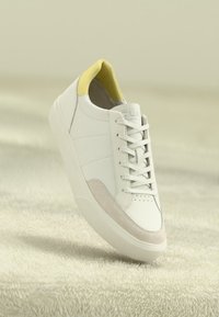 Sneaker in pelle bianca con un tallone giallo e accenti in suede grigio chiaro. Presenta un design a profilo basso e punta tonda con chiusura a lacci.