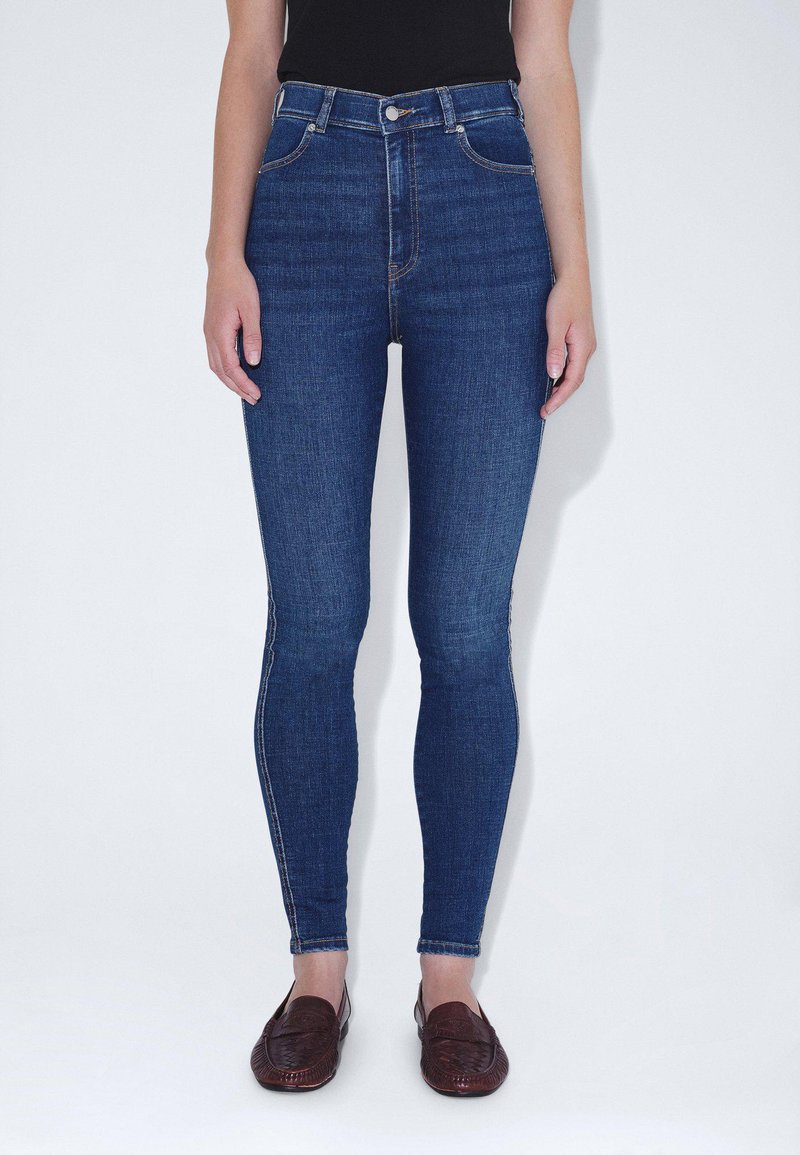 Jeans de mezclilla azul de cintura alta con un corte ajustado, que incluyen bolsillos frontales y un cierre de cremallera clásico. Textura suave con mínimas costuras.