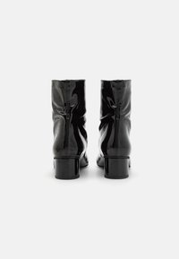 Botas de tobillo de charol negro con un diseño arrugado, tacones de bloque de altura media y detalle de cremallera en la parte trasera. Textura suave.