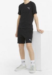 Schwarzes Baumwoll-T-Shirt und Shorts-Set mit kleinem weißem Puma-Logo. Socken und Sneakers vervollständigen den Look, mit leichter Textur und figurbetontem Design.
