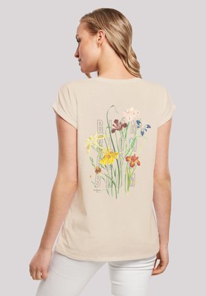 Beige T-Shirt mit kurzen Ärmeln und floralem Design auf der Rückseite, mit dem Wort "BLOOM". Weicher Stoff mit lässiger Passform und umgeschlagenen Ärmeln.