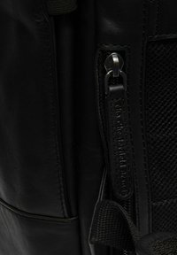 Mochila de cuero negra con un panel lateral texturizado, cremallera de metal, costuras decorativas y acentos de malla en contraste.