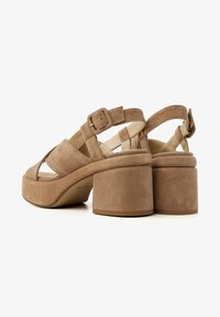 Beige suede platform sandals with a chunky heel, featuring multiple straps and a side buckle for adjustment. Textured upper with stitching details.