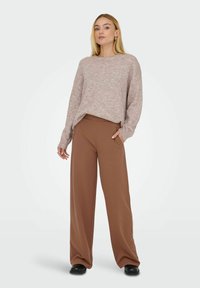 Lyserød, struktureret sweater med rund hals og lange ærmer, parret med løse, brune bukser med højt liv og sorte sko.