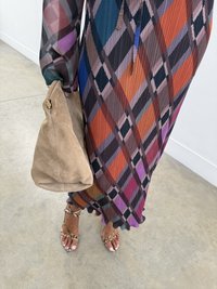 Rochie pliată colorată, cu un model de carouri diagonale în nuanțe de roșu, albastru și violet, asociată cu o geantă din suede bej și sandale metalice.