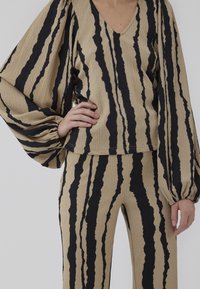Beige and black striped knit outfit, featuring a V-neck, balloon sleeves, and textured fabric. Tailored fit with contrasting pattern details.