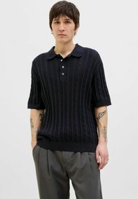 Polo shirt tricotat de culoare bleumarin cu un model de cabluri, mâneci scurte și guler cu trei butoane. Purtați-l cu pantaloni gri.