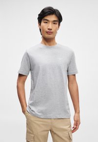 Pelēka īsām piedurknēm t-kreklu, izgatavots no mīkstas, gludas materiāla ar apaļu kakla izgriezumu un nelielu, diskrētu logotipu uz krūtīm.