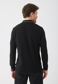 Svart långärmad polo med krage och kontrasterande kanter. Tillverkad av ett mjukt tyg, figursydd design, synliga söm detaljer.