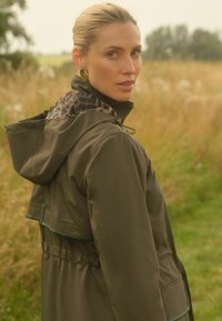 Zelená nepromokavá bunda s kapucí na stažení, staženým pasem a podšívkou s leopardím vzorem. Obsahuje kapsy a kontrastní lemování.