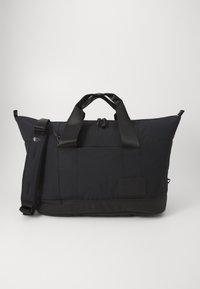 Black duffel bag with nylon material, rectangular shape, dual top handles, adjustable shoulder strap, and logo patch on the side.