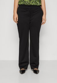 Black, wide-leg trousers with an elastic waistband, paired with a patterned green top. Footwear features pointed toes with decorative buckles.