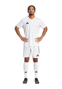 Witte voetbalshirt met een textuur van geometrische patronen, zwart adidas-logo, gecombineerd met witte shorts en hoge witte sokken. Zwarte voetbalschoenen.