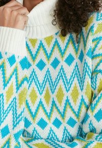 Gebreide trui met een hoge, geribde kraag. Het ontwerp bevat een ruitpatroon in turquoise, limoengroen en wit.