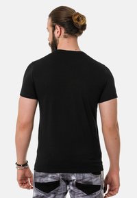 Schwarzes T-Shirt mit kurzen Ärmeln und einem klassischen Rundhalsausschnitt. Der Stoff wirkt glatt; das Design zeichnet sich durch eine figurbetonte Silhouette ohne sichtbare Akzente aus.