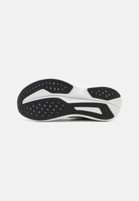 Semelle de chaussure de sport noir et blanc avec un motif de grip texturé et des découpes circulaires. Présente un contour élégant avec des détails de logo.