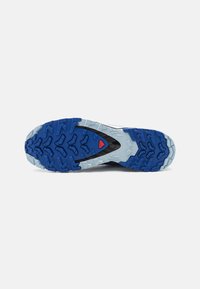 Semelle de chaussure en caoutchouc bleu et gris, avec un motif de grip texturé et des accents noirs. Présence d'un logo en relief et d'un accent rouge sur le dessous.