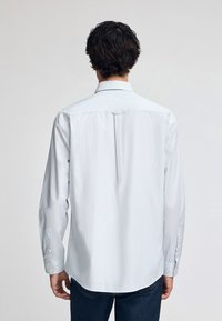 Ljusblå och vit randig skjorta, med knäppning, lång ärm med knappmanschetter och en lätt rundad nederkant. Slät tygkvalitet.