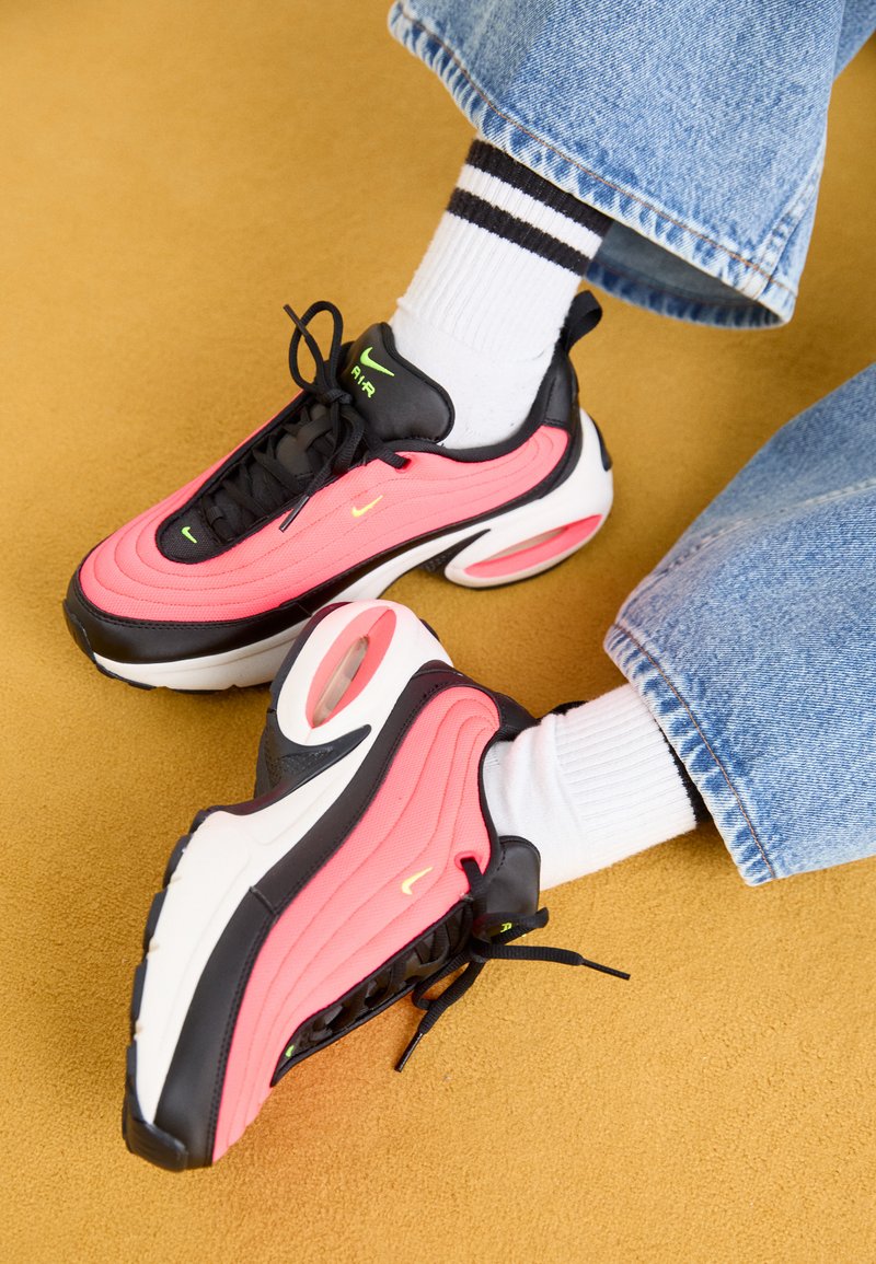 Black and pink sneakers with wavy design, featuring white sole and visible air unit, complemented by black laces and green accents.