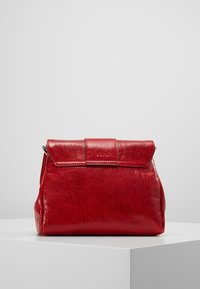 Sac à main en cuir rouge à forme structurée, avec un rabat pliant et une texture lisse. Design minimaliste avec des détails de couture subtils.