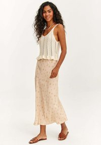 Krémový pletený top s tenkými ramienkami a zúženým lemom, v kombinácii s voľnou béžovou sukňou s jemným kvetinovým vzorom. Hnedé šľapky.